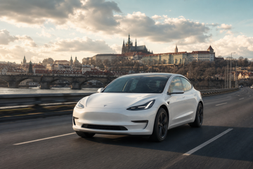 Tesla Model 3 driving on Czech highway near Prague with medieval skyline in background