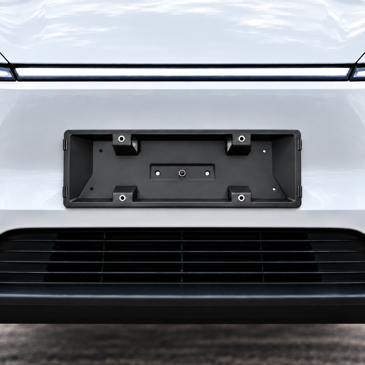 A black metal license plate frame mounted on the front bumper of a white vehicle, shown against a clean outdoor background.