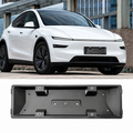 A white electric vehicle is shown in an outdoor urban setting, with a black rectangular license plate frame product displayed below on a plain white background.