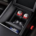 A black car center console organizer tray with a sliding drawer and cup holders, shown open with two red cans and a pair of eyeglasses inside. The tray is installed in a dark car interior.