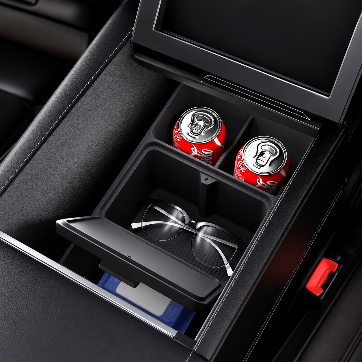 A black car center console organizer tray with a sliding drawer and cup holders, shown open with two red cans and a pair of eyeglasses inside. The tray is installed in a dark car interior.