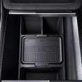  A black textured car center console organizer tray with a lid, shown installed inside a dark car console compartment.                                                     