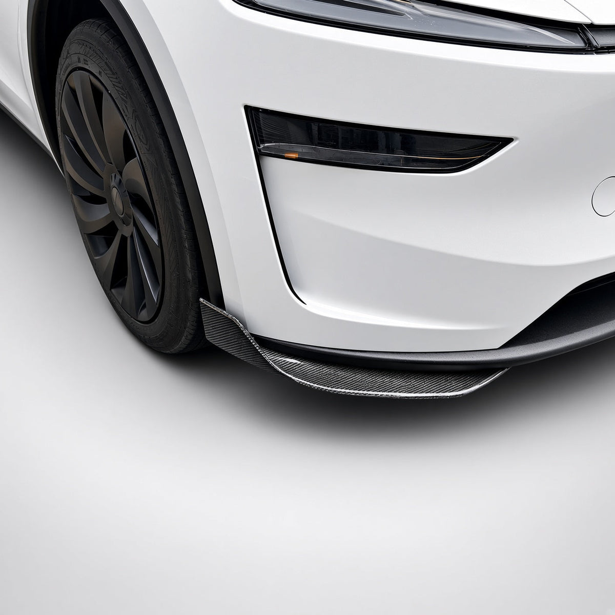 Carbon-fiber lower bumper corner trim fitted near the front wheel of a white Model Y Juniper