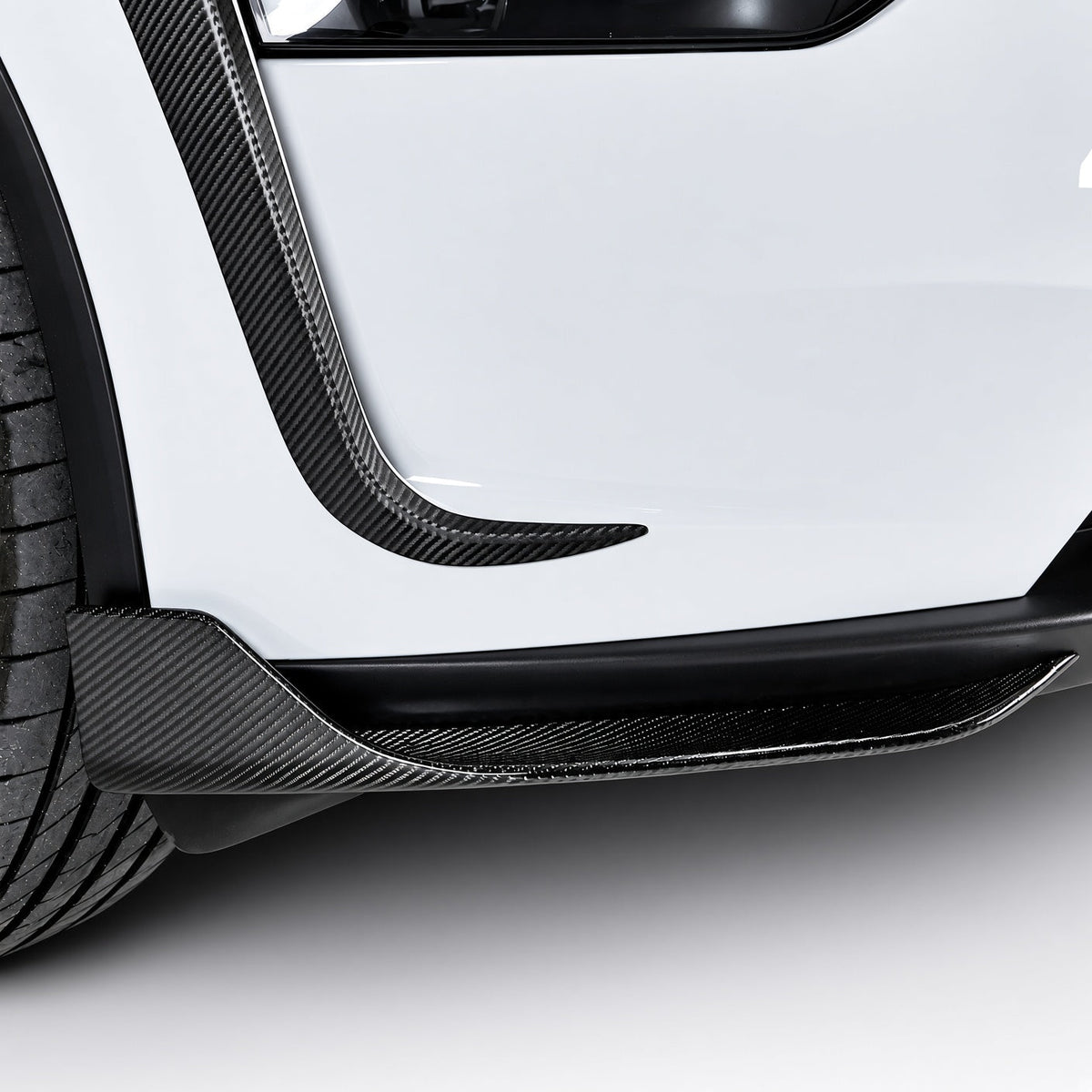 Close-up of carbon-fiber lower bumper corner trim beside the front tire